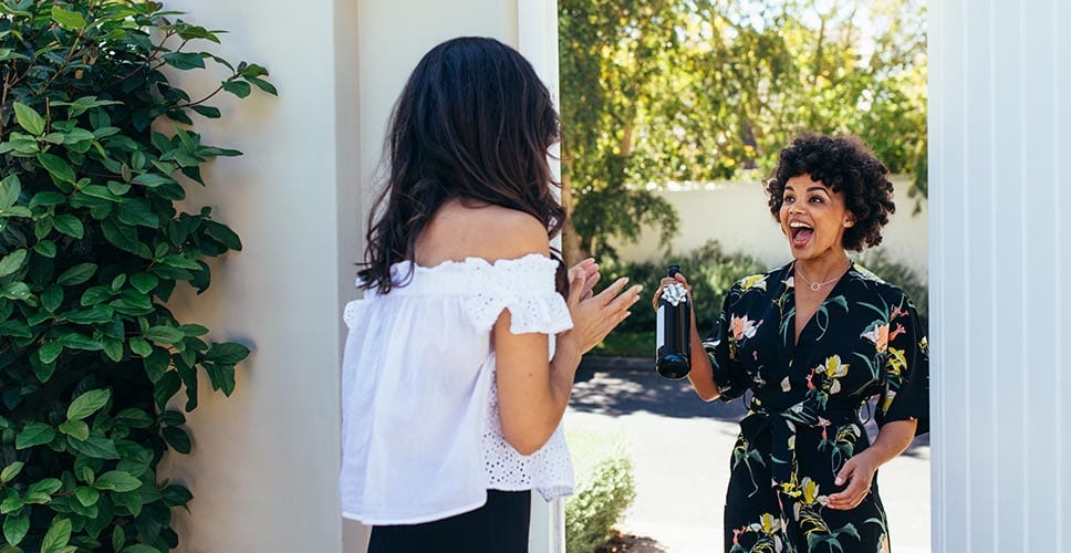 Two young women greet each other at a housewarming party.