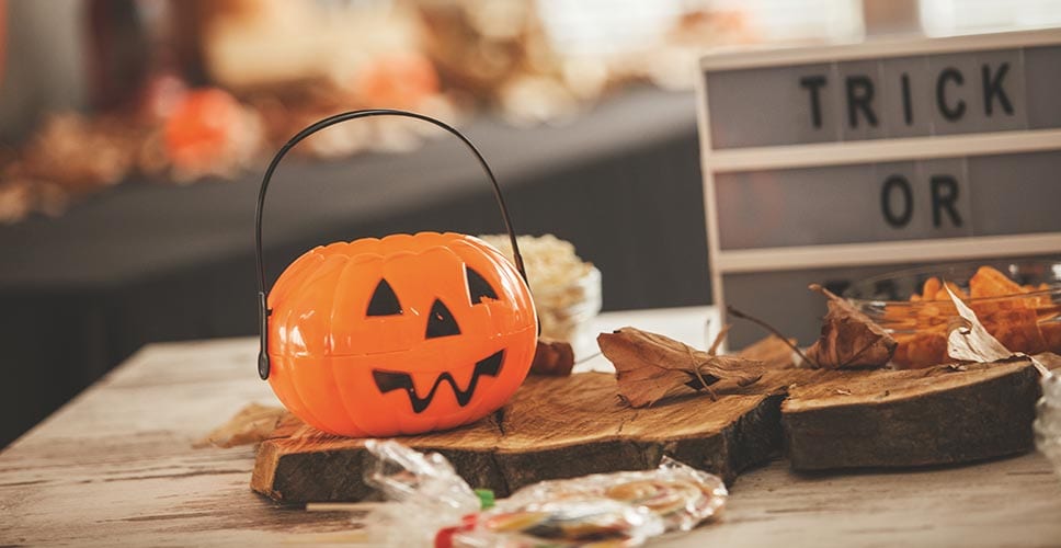 A table decorated for Halloween with a trick or treat sign and a jack-o-lantern basket for candy.