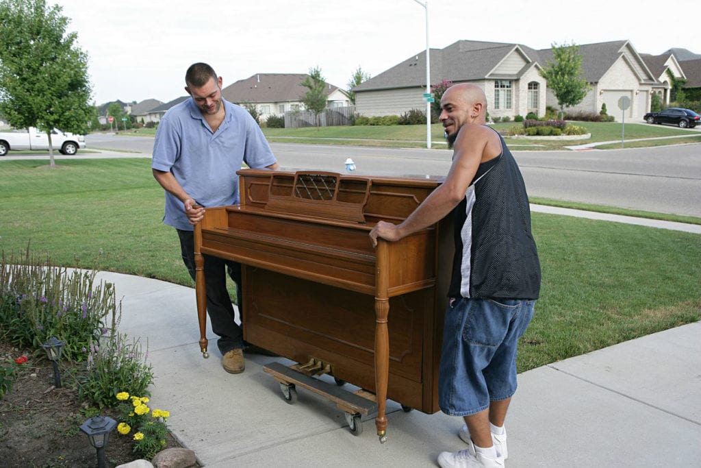 Professional movers help transport a valuable piano into a new home.