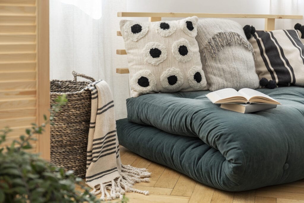 Books on scandinavian futon with pillows in elegant bedroom interior, real photo