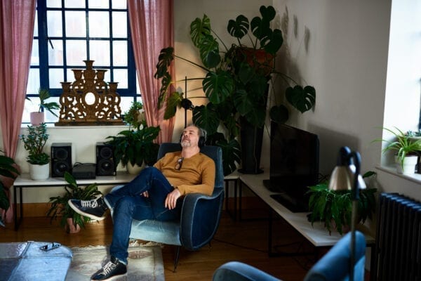 Man sitting in armchair wearing headphones in living room, calm, solitude, escapism