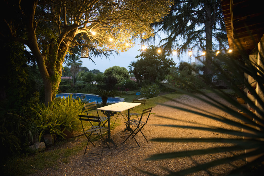 A garden dining table lit up with cafe lights at night.