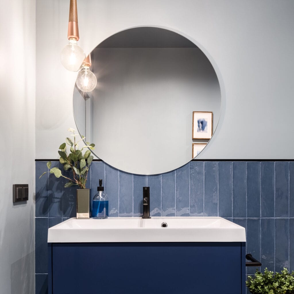 Designed bathroom with stylish blue cabinet, blue wall tiles and big round mirror affordable bathroom décor