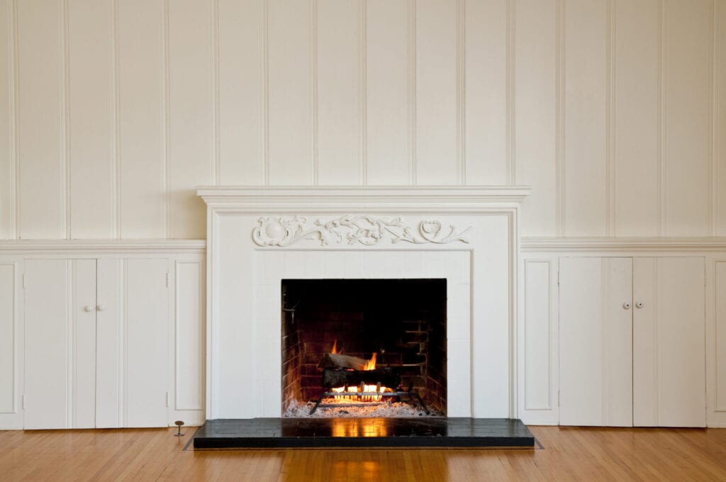 Traditional fireplace with floral relief moulding in empty domestic room. There is a real roaring fire in the fireplace.