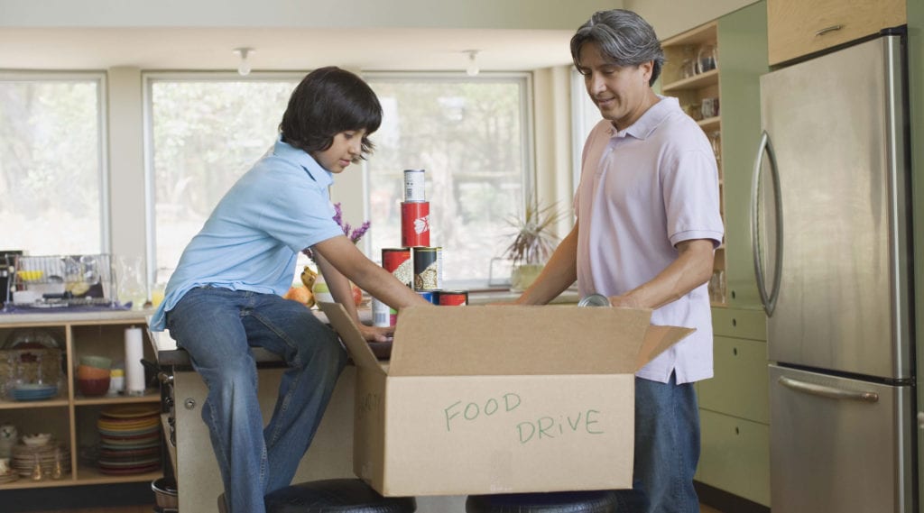 Father and son pack canned goods into a moving box labeled "donations"