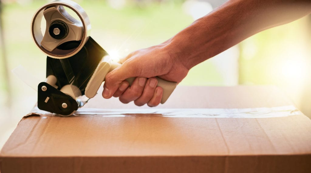 Closeup shot of a hand closing a cardboard box with tape during a move.