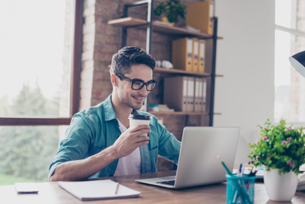 man holding coffee using laptop