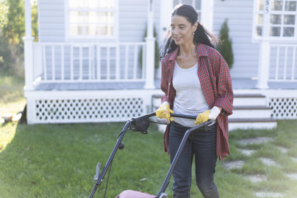 Woman mows the lawn with an electric mower, back yard.