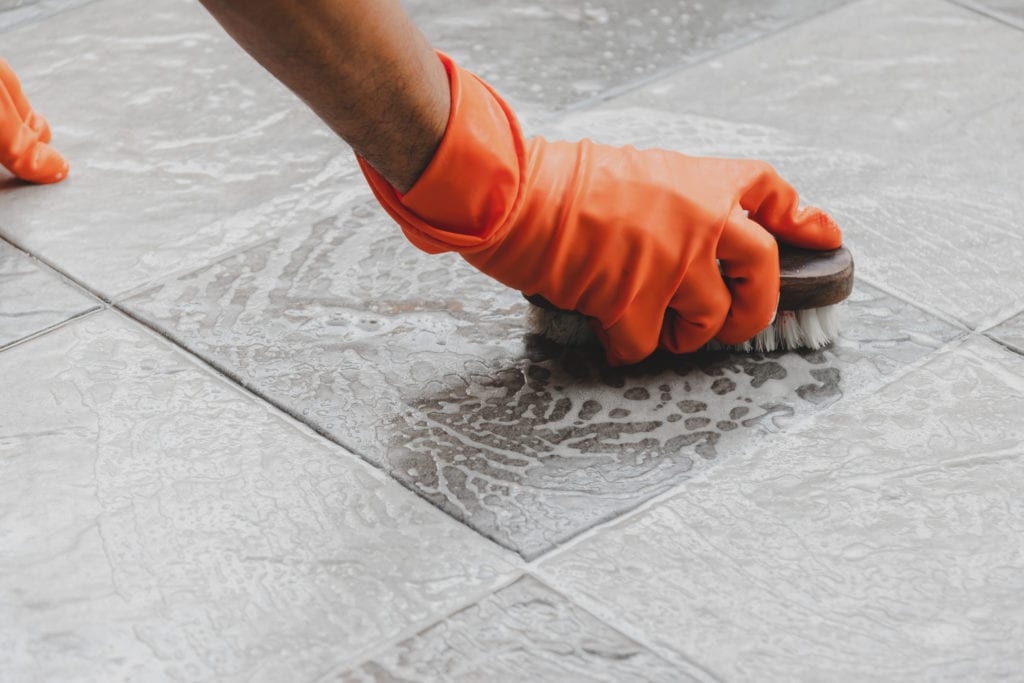 Person with orange rubber gloves is scrubbing bathroom floor