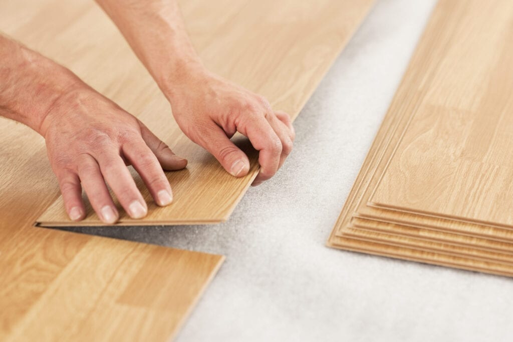 Man laying laminate flooring planks. Oak effect planks being placed over insulating foam underlay.