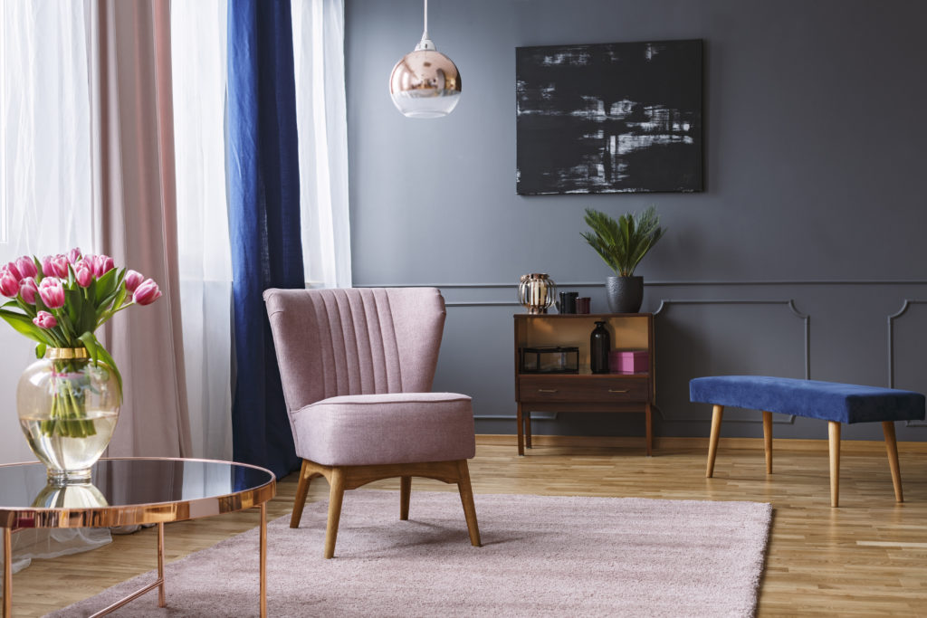 Pink armchair standing on a rug and under a lamp in living room with gray walls