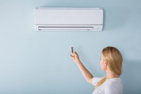 woman operating wall air conditioning unit with remote control