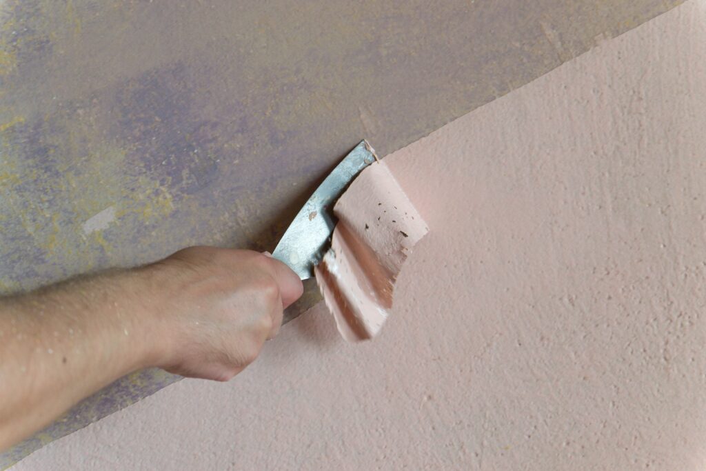 Close up worker hand scraping old paint on concrete wall.