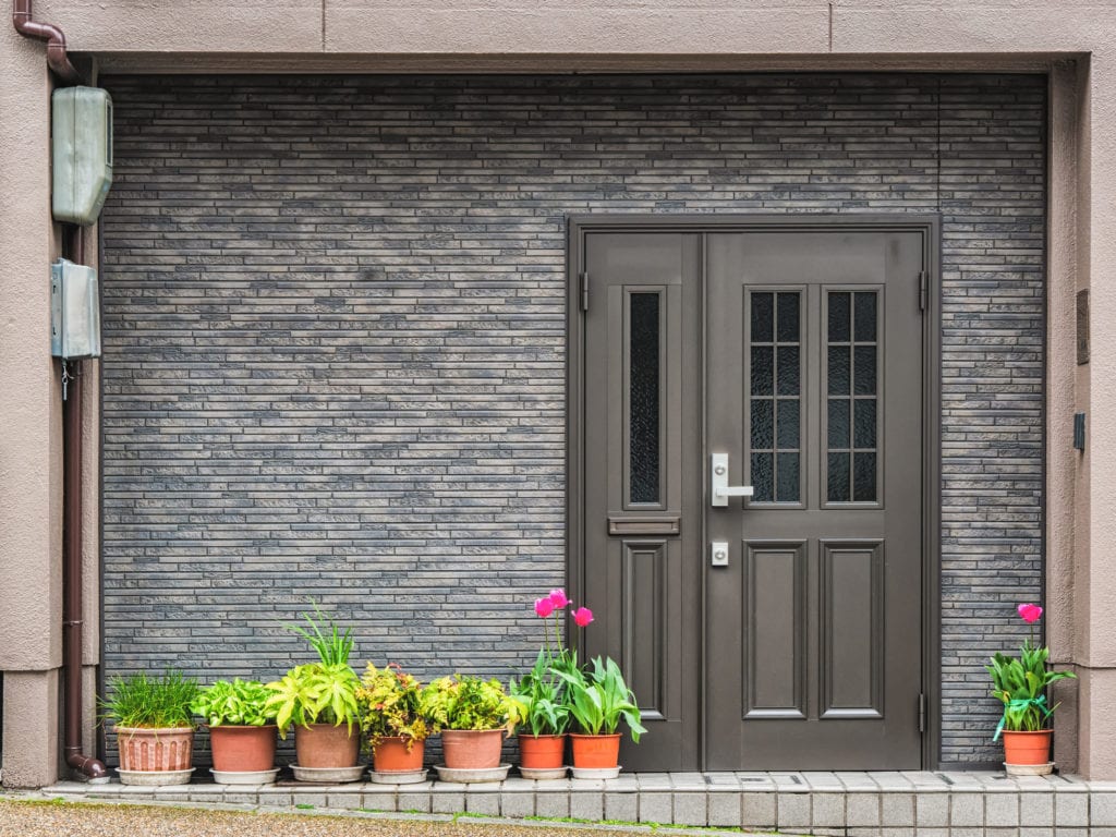 Gray front door with small square decorative windows and flower pots in front of it