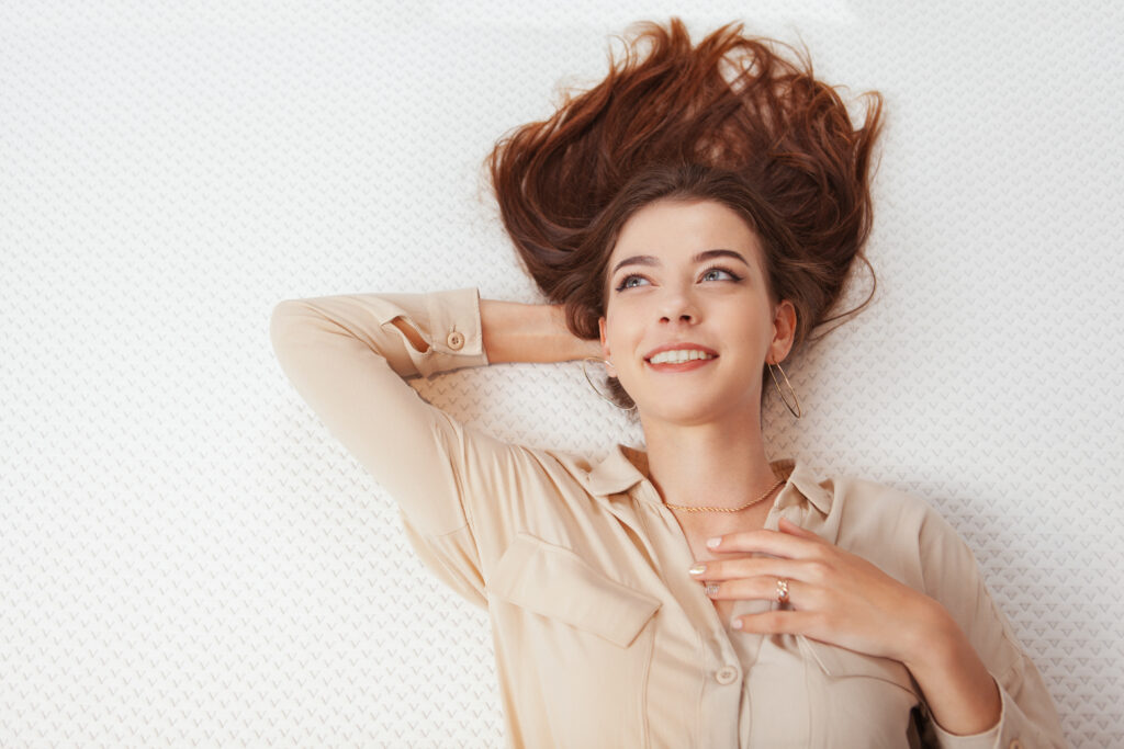 Top view shot of a happy woman smiling, lying on orthopedic mattress, copy space. Healthy sleep, relaxation concept