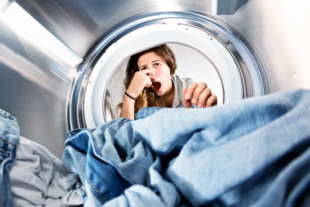 Laundry left in dryer stinks! Unhappy woman holds nose.