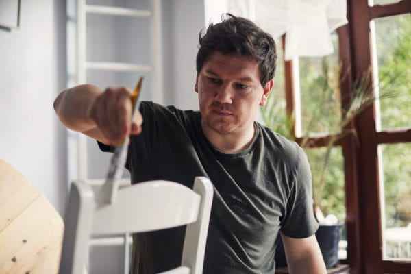 Man painting a chair at home in the living room