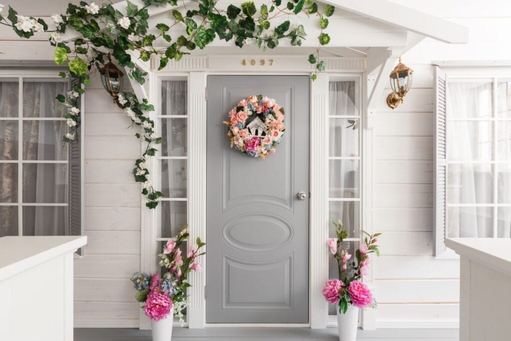 Entrance of home with light gray door, wreath, and spring flowers