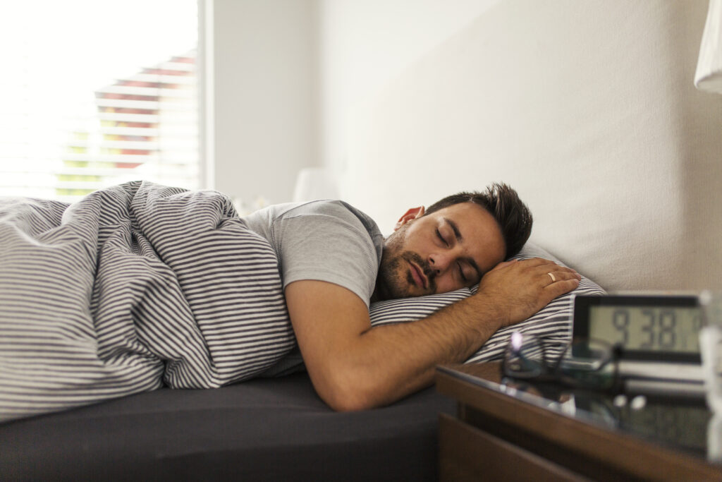 Handsome man sleeping in his bedroom. Man sleeping with alarm clock in foreground.