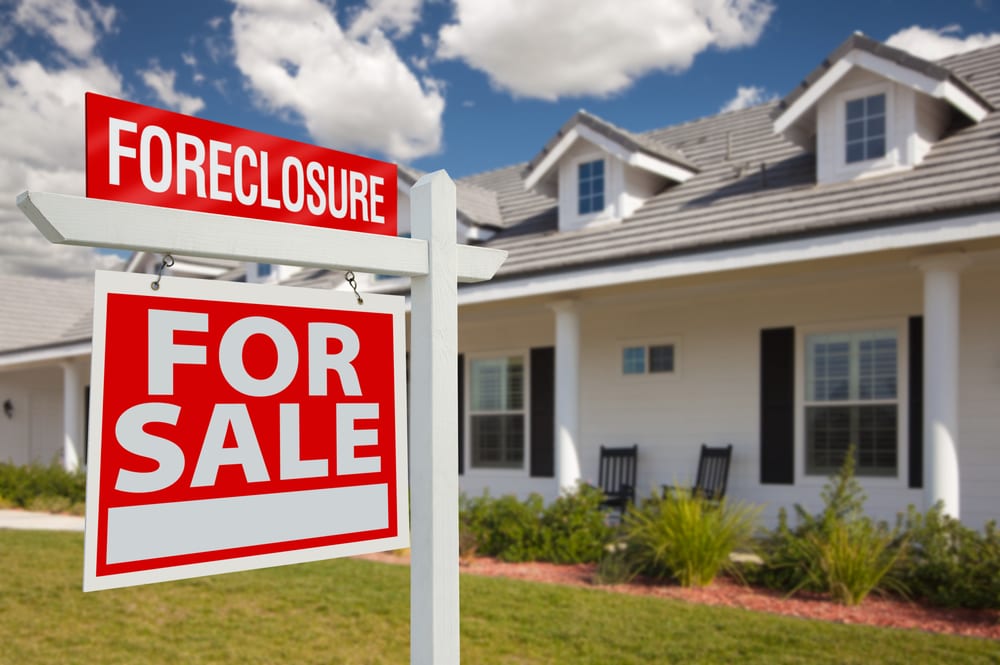 A white home with a foreclosure for sale sign out front