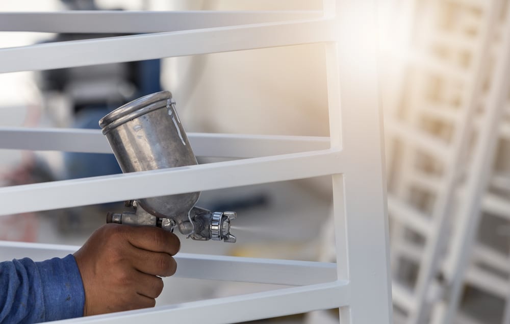 Man using a paint sprayer to paint a steel fence white