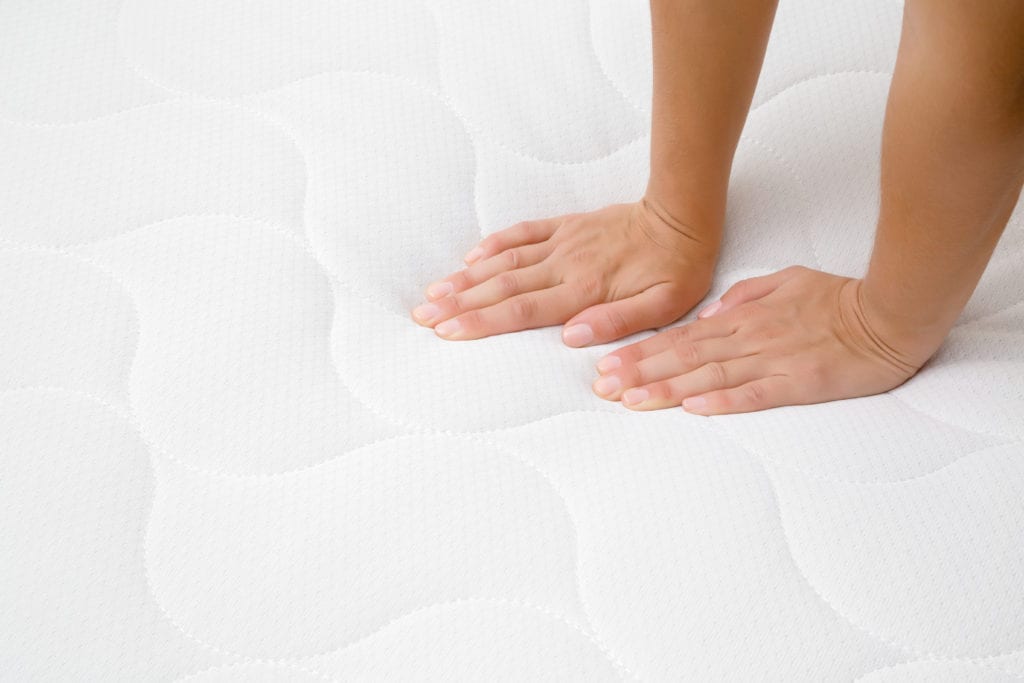 Woman's hands pressing on white mattress