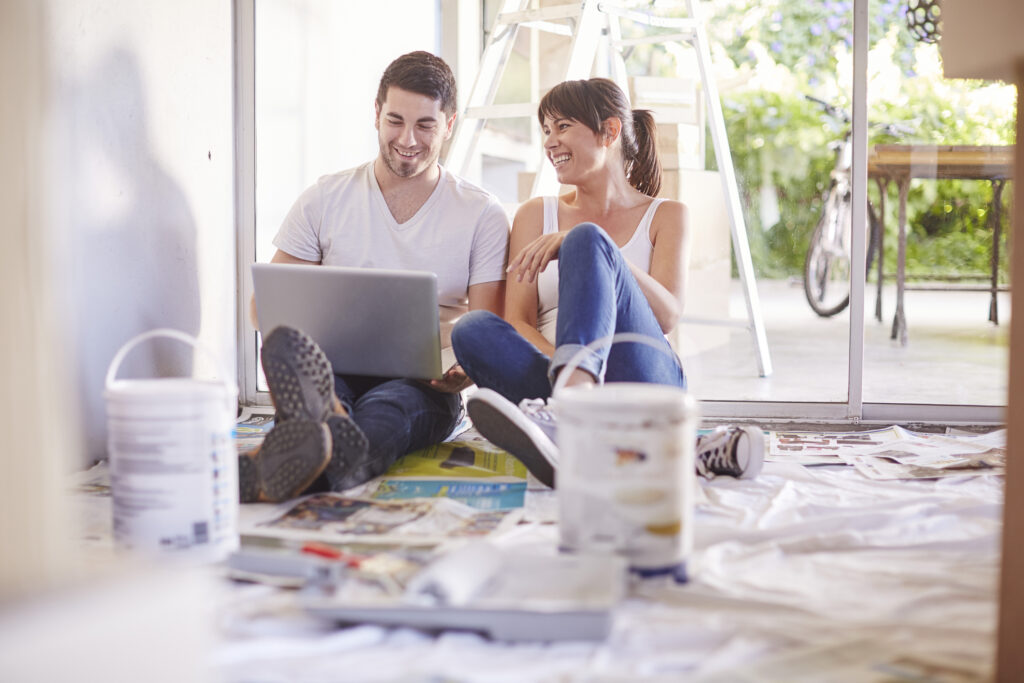 Couple moving house, relaxing after paintig and looking on a laptop