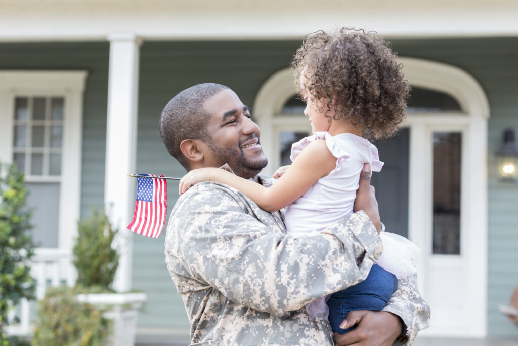 Happy mid-adult soldier picks up his preschool age daughter as he returns home from assignment.