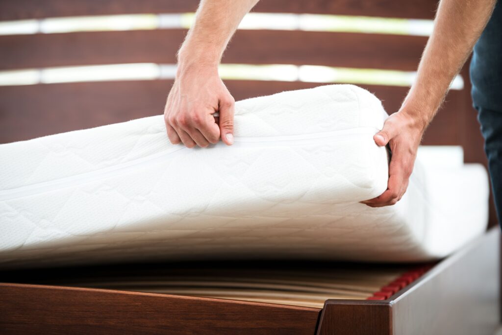 Close up photo of man lifting mattress off of bed