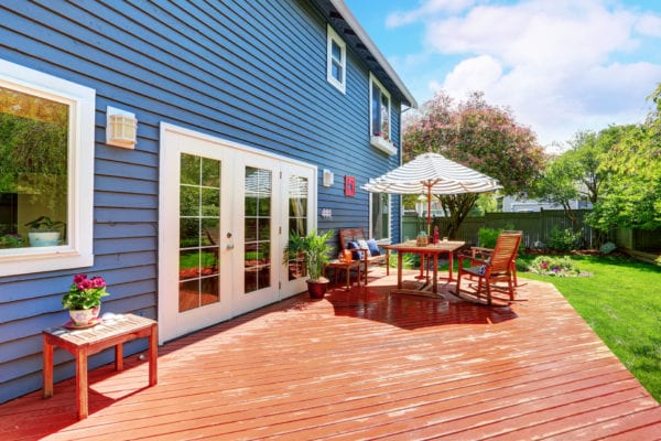 Wooden walkout deck in the backyard garden of blue siding house. Furnished with patio table set with umbrella