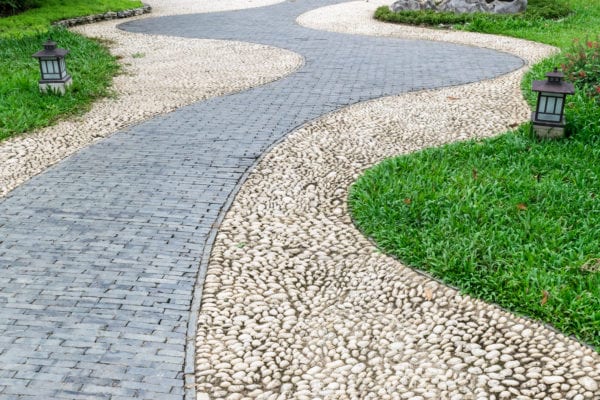 stone and brick walkway pavement in garden pass through grass field with two lamp lighting on ground beside the way