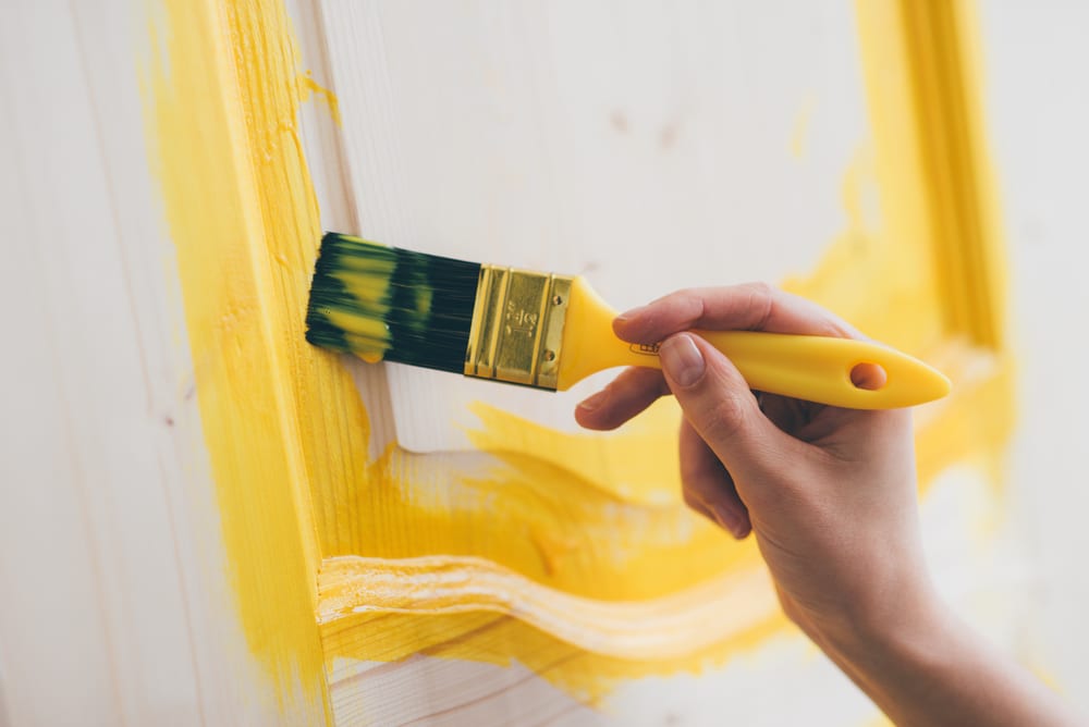 A close-up of a woman's hand painting a door yellow