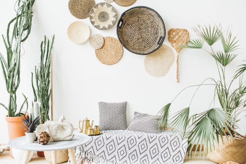 Modern minimal home interior design. Pillows, golden teapot, decorative straw plates, Scandinavian blanket, tropical palm tree, succulent and decorations.