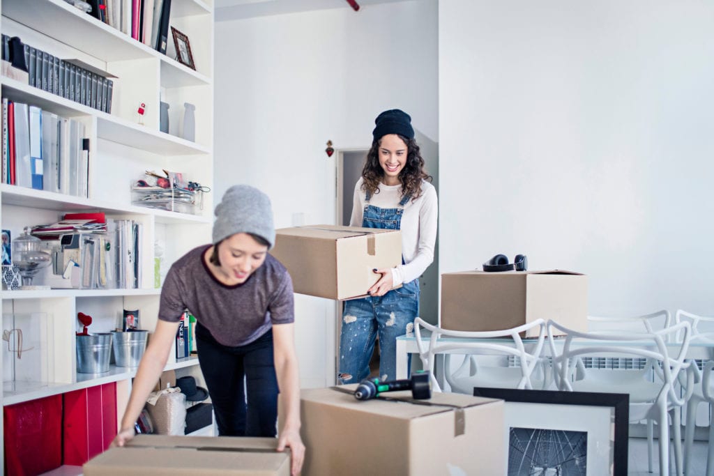 Young couple carrying cardboard boxes. Smiling homosexual females are moving into new house