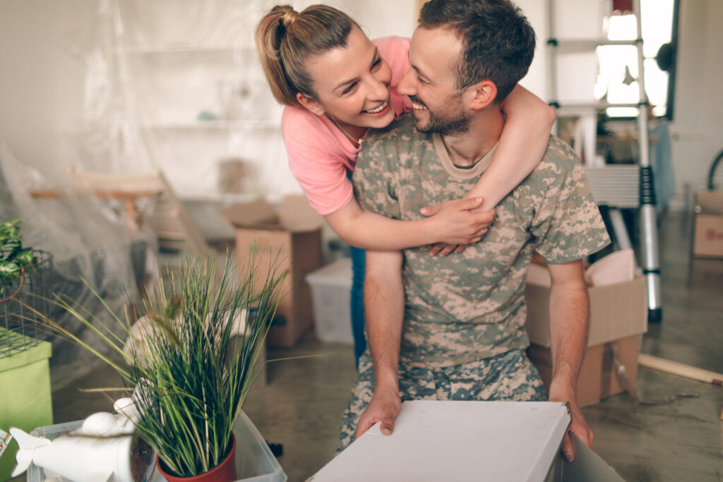 Photo of a young man in a soldier uniform, moving into a new apartment with his wife