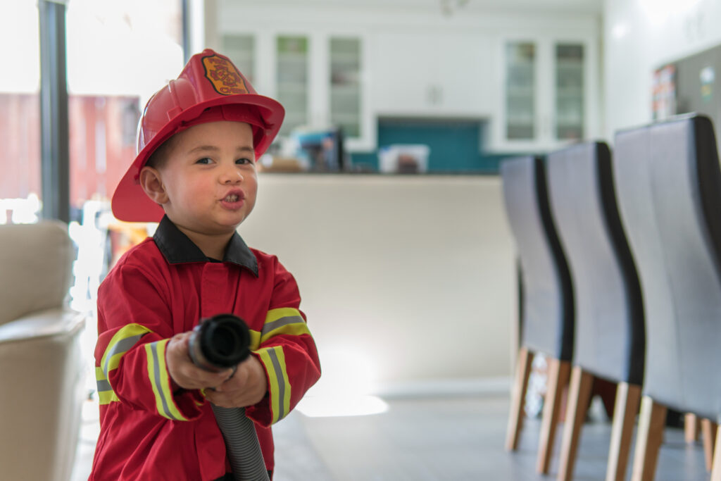 little boy in firefighter uniform wields a fire hose