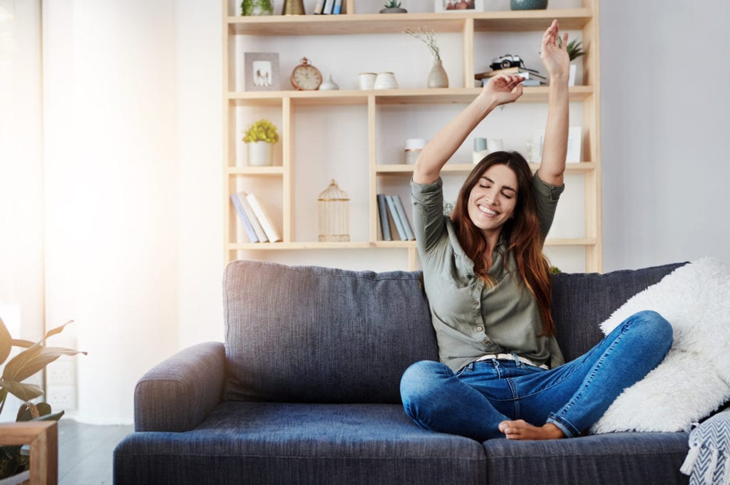 Shot of a happy young woman dancing while sitting on her sofa at home