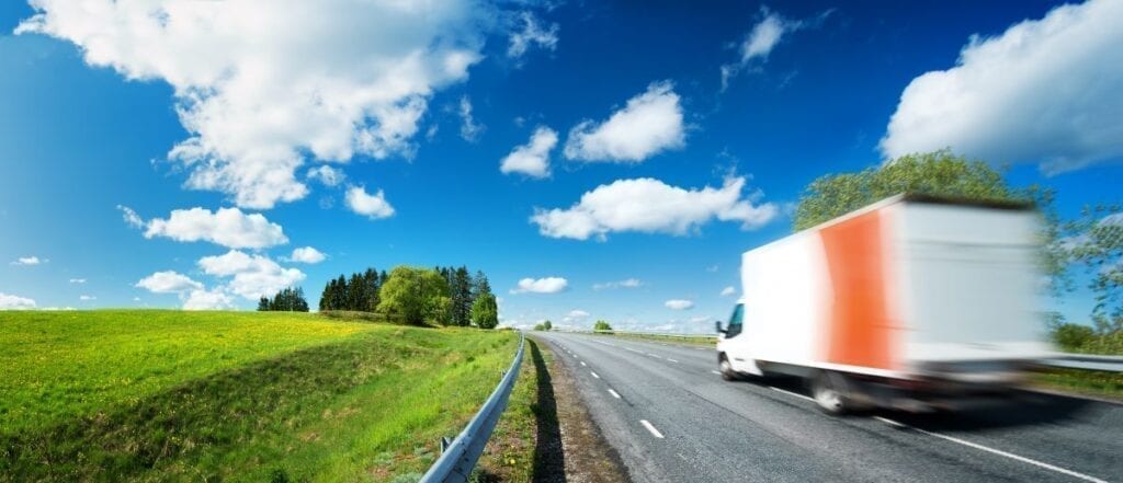 Moving truck driving on highway next to green field