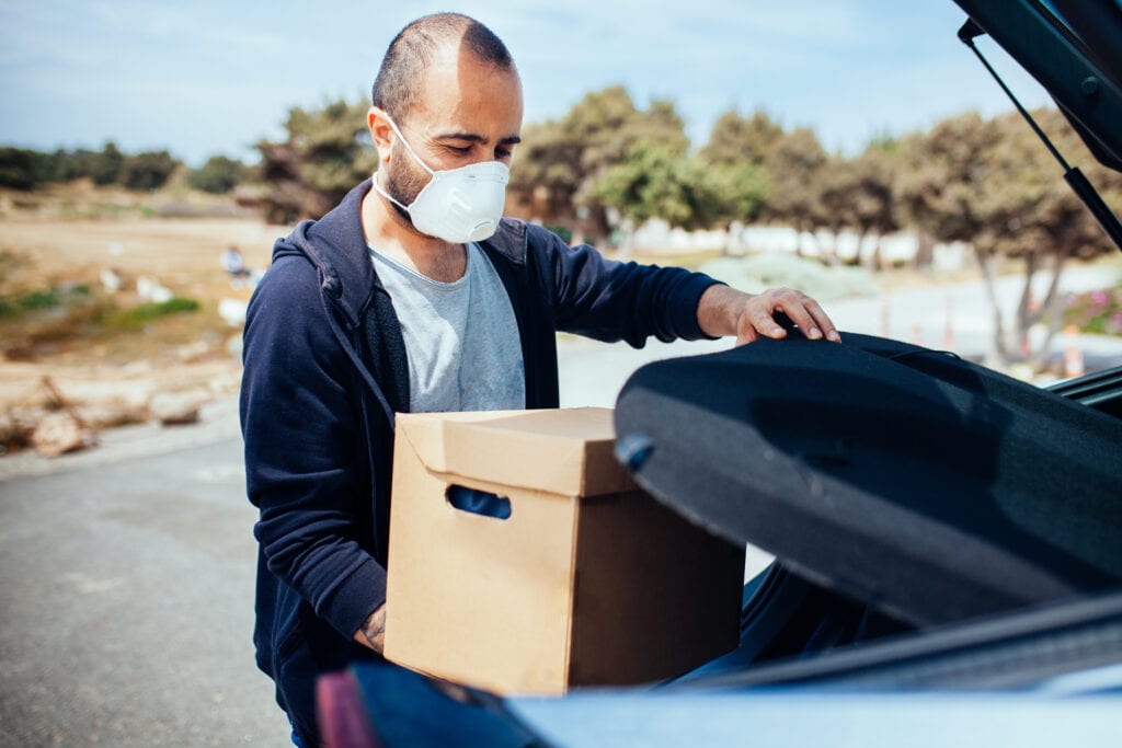 Man carrying box from his car, wearing protection mask