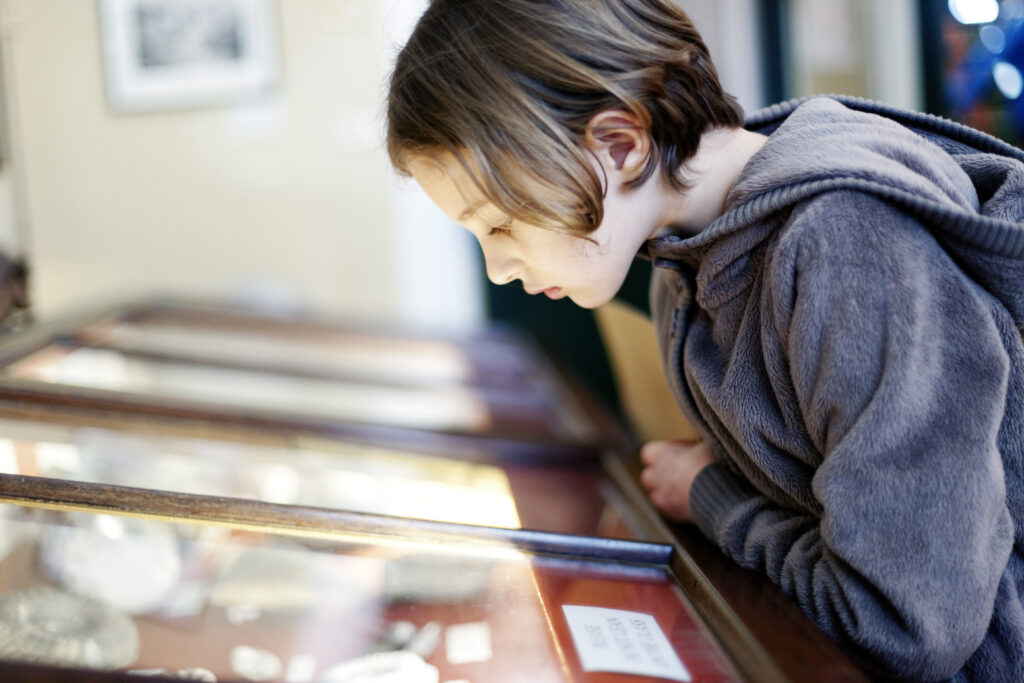 A young girl looking at an exhibit in a glass display case in a museum, Lyme Regis, Dorset, UK