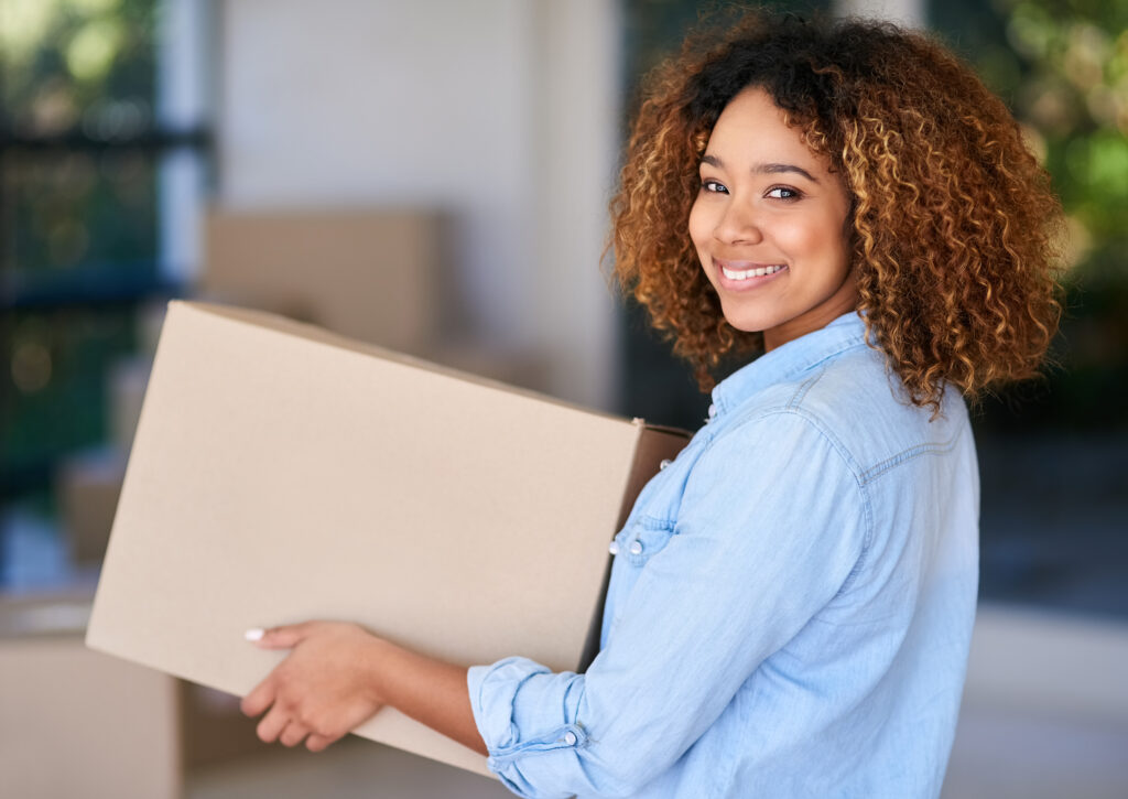 Portrait of a young woman carrying a cardboard box into her new home