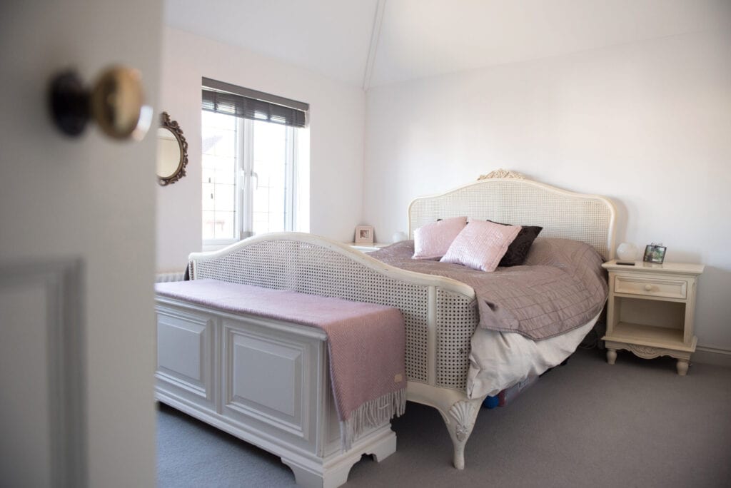 A general interior view of a bedroom with old cream Louis style wicker double bed with satin bedspread within a home.