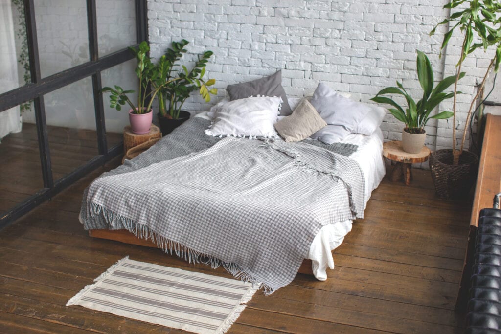 Eclectic bedroom interior with tropical plants. White brick wall and wooden floor.