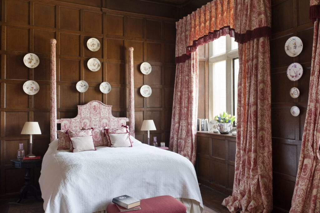 Toile de jouy curtains and bed dressings by Design Archive in bedroom with wooden wall panelling and decorative china plates