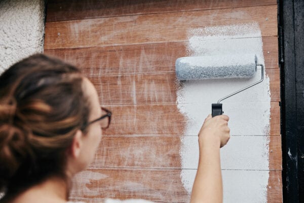 A woman using a paint roller, painting wooden planks on a wall.