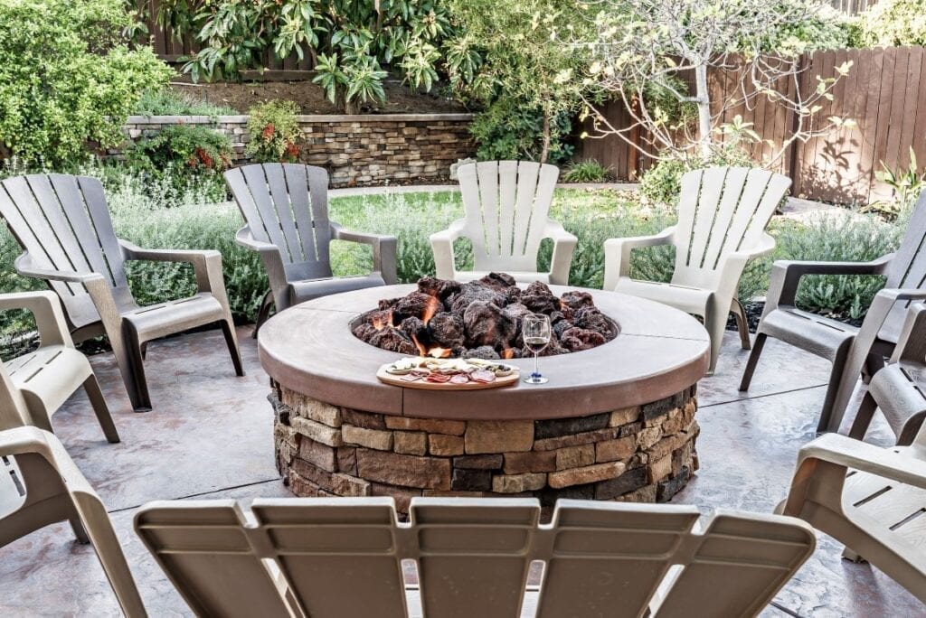 Backyard fire pit surrounded by Adirondack chairs