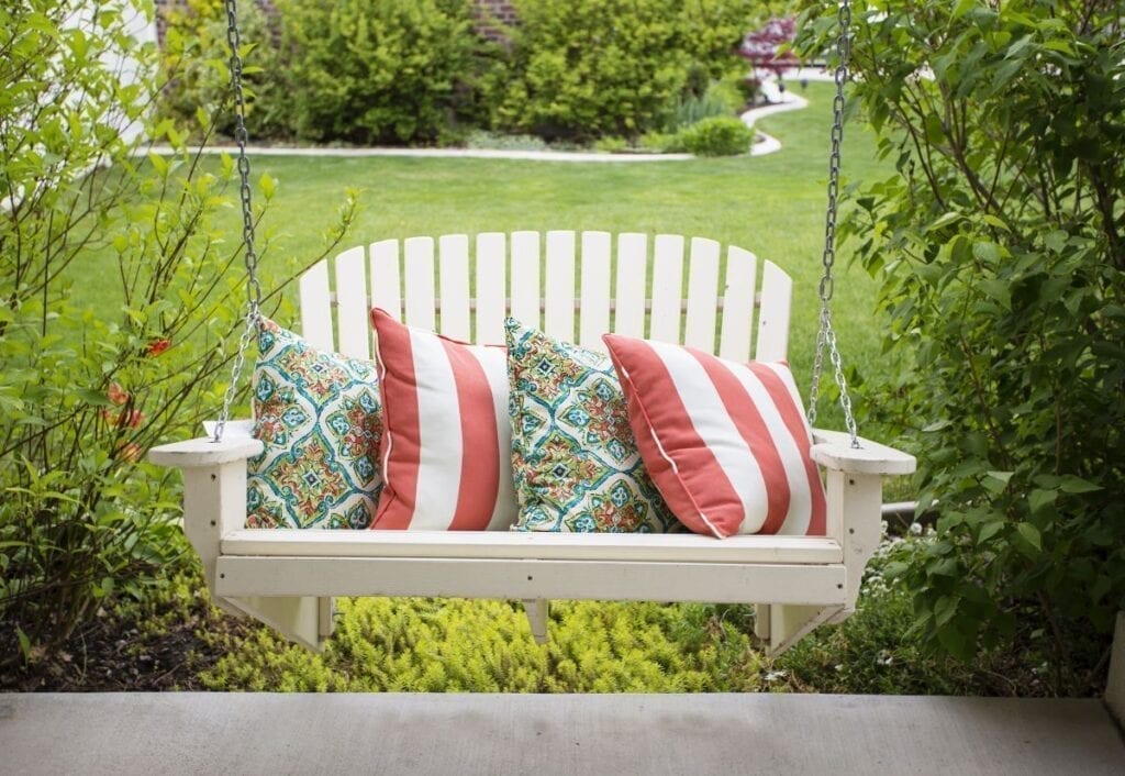 White porch swing with pillows in front yard