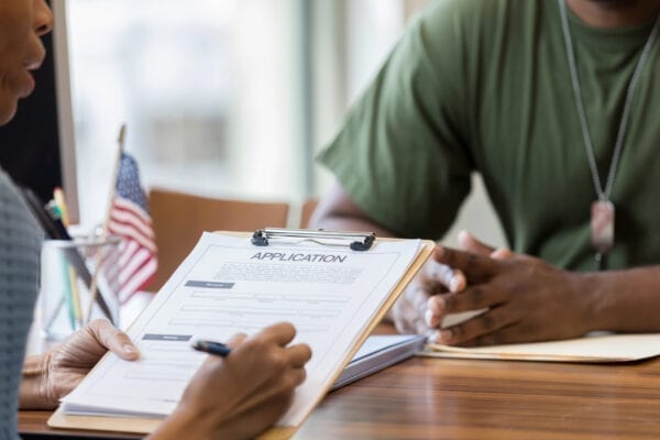 A mid adult African American bank manager fills out a loan application while an African American soldier looks on.