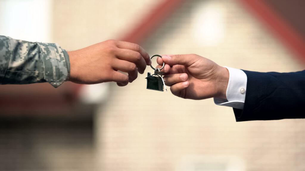 Man in business suit giving house key to man in military uniform, state support