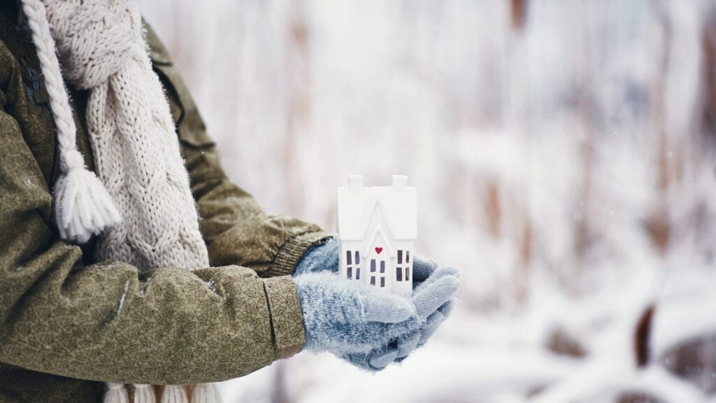 Female hands holding tiny house in snowy weather